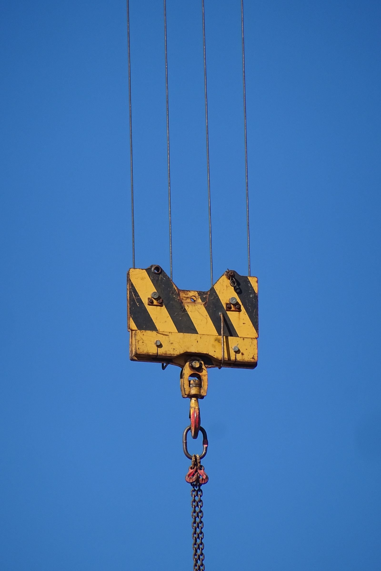 Crane hook block suspended by wire ropes against a blue sky